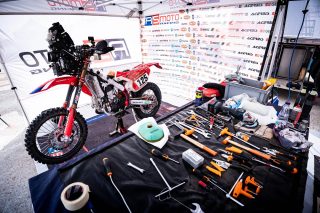 テントの下で整備中の赤いレーシングバイク「125番」と工具