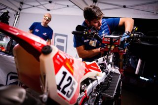テントの中で125番の赤いダートバイクを整備する男性