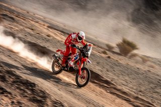 砂漠の荒野を赤いホンダのオフロードバイクに乗ったライダーが疾走