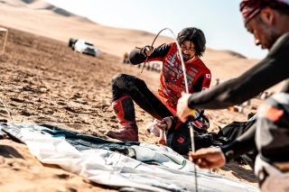 砂漠のような乾いた土地で、二人の男性がテントのようなものを組み立てる