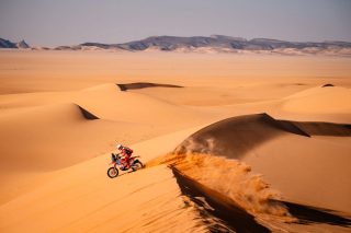 広大な砂漠の砂丘をオフロードバイクで走行するライダー
