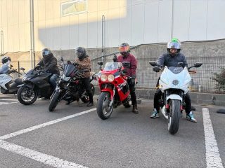 数台の様々なタイプのバイクが駐車場に並び、ライダーたちがヘルメットを着用して座ったり立ったりしている