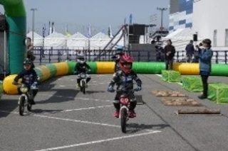 子供たちがヘルメットを着用し、電動バイクに乗って屋外のコースを走行している様子