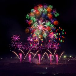 夜空を彩る壮大な花火大会の様子。多種多様な色鮮やかな花火が打ち上がり、地上には噴水のような花火も見え、祝祭的な雰囲気を醸し出している。