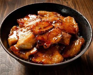 黒い器に盛られたご飯の上に、照り焼き風のタレがたっぷりかかった香ばしい豚肉がのった豚丼