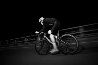 夜の橋の上をロードバイクで走行する人物を捉えたモノクロ写真