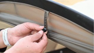 手がテントや日よけのような生地に付いている小さなクリップを調整している様子