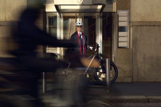 スーツ姿の男性が自転車を携えて建物エントランスに立つ