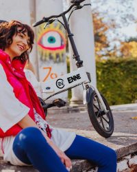 女性が白い折りたたみ電動自転車の隣で笑顔で座っています