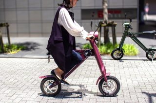 舗装された街路で、女性が紫色の電動スクーターに乗って移動しています