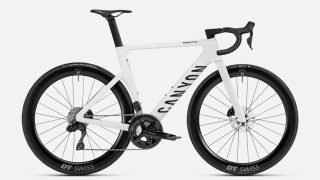 白い背景に置かれた、CANYON AEROAD CF SLXというモデルの白いロードバイクです。DT SWISSのホイールとSHIMANO 105のコンポーネントを搭載しており、空気抵抗を考慮したエアロ形状が特徴の高性能なスポーツ自転車です。