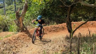青いヘルメットをかぶった子供が、赤いマウンテンバイクに乗ってダートトラックを走っている様子。