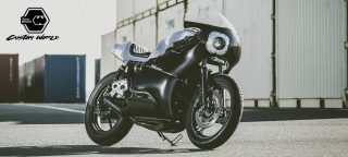 工業地帯のコンテナを背景に、マットブラックのカスタムされたカフェレーサースタイルのバイク