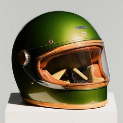 メタリックグリーンのレトロなフルフェイスヘルメットが白い台座に置かれています