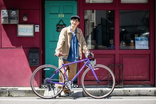 紫色の自転車に寄り添って笑顔を見せる若い男性
