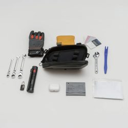 白い背景に、手袋、各種工具、バッグ、財布、AirPods、懐中電灯、鍵などの個人用品や道具が整然と並べられています。