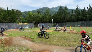 自然豊かな屋外のコースで、ヘルメットを着用した大人と子供たちがマウンテンバイクを楽しんでいる様子