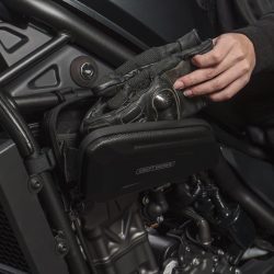 バイクのフレームに取り付けられた収納ケースに、ライダーが黒いグローブを出し入れしている様子。