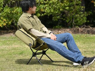 草地でオリーブ色のポータブルキャンプチェアに座ってリラックスする男性