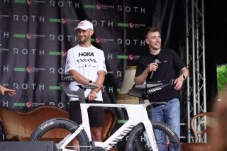 ステージ上で白いタイムトライアルバイクを囲む男性たち