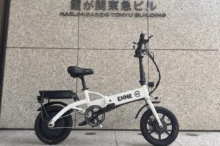 霞が関東急ビルの前で、白い折りたたみ式の電動自転車が壁を背景に停められている様子を捉えた画像です。自転車には「ENNE EV」のロゴが見えます。