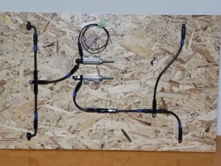 OSBボードに黒いホースやチューブ、金属製フィッティング、センサーのような部品が複雑に配置されたシステムが取り付けられています。