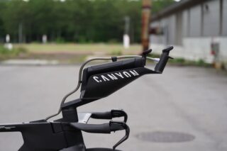 黒いCANYONブランドのタイムトライアルバイクのハンドル部分をクローズアップした画像。エアロバーやブレーキレバーなどの詳細なコンポーネントが写っており、屋外の舗装路が背景となっています。