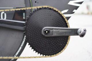 高性能な競技用自転車のドライブトレイン部分をクローズアップ。SRAM REDクランク、Quarqパワーメーター、エアロディスクチェーンリング、ゴールドチェーンが特徴的。精密なコンポーネントが強調されている。