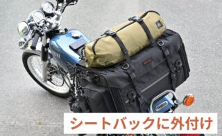 青いYAMAHAのバイクのリアシートに、黒い大型のシートバッグとカーキ色のロールバッグがしっかりと固定されています。ツーリングやキャンプに適した荷物積載状態を示しており、「シートバックに外付け」という文字が見えます。