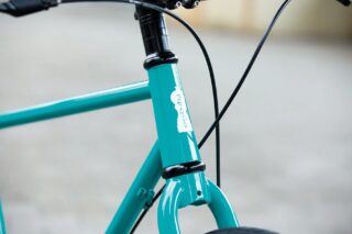 ターコイズブルーの自転車のフレームとフロントフォーク部分をクローズアップした画像です。ヘッドチューブには「rep cycles」というロゴが白字で書かれています。ハンドルバーとブレーキケーブルの一部も見えます。