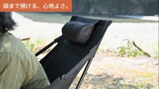 屋外で、頭までしっかり支えるヘッドレスト付きのキャンプチェアに座り、くつろぐ人物の画像です。川辺のような場所で快適に過ごしている様子が伝わります。