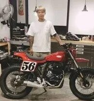 ガレージで赤いカスタムバイクの隣に立つ男性