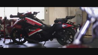 赤と黒のスポーティなデザインのオートバイが、工具が置かれたガレージのような屋内に駐車されています