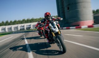 赤いレーシングスーツとヘルメットを着用したライダーが、白いドゥカティのスポーツバイクでサーキットを高速で走行している様子