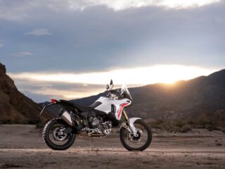 白いドゥカティ・デザートXが、夕焼けに染まる広大な荒野に停車している