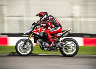 赤と白のレーシングスーツを着たライダーが、ドゥカティのスーパーモトスタイルのバイクでサーキットを高速走行している様子
